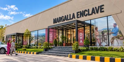 Margalla Enclave Islamabad sales office exterior featuring modern glass architecture, landscaped gardens, entrance steps, and property development displays.