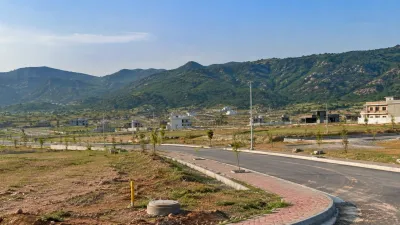 Developing residential area with paved roads, vacant plots, modern houses, and Margalla Hills in the background, illustrating property development in Margalla Enclave Islamabad.