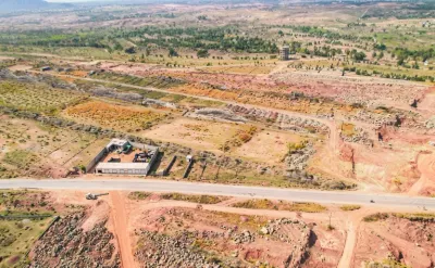 Aerial view of Faisal Town Phase 2 showing a carpeted road, levelled plots, rock piles and a water tank under development