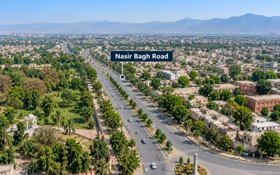 Aerial view of Nasir Bagh Road in Peshawar showing a multi-lane highway, surrounding green parks, residential areas, and mountain ranges in the background.