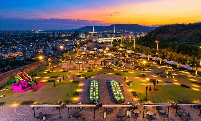 Illuminated hilltop park overlooking Islamabad with Faisal Mosque and Margalla Hills at sunset.