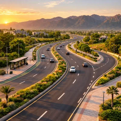 Wide landscaped boulevard in Islamabad with light traffic, a bus stop, green medians, and Margalla Hills in the background at sunset.