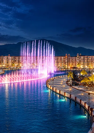 Illuminated musical fountain and waterfront promenade at Park View City Islamabad, with residential buildings and hills in the background at night.