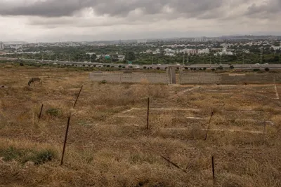 Stalled Islamabad sector E-13 with empty overgrown plots, survey stakes and unfinished wall with the city and Islamabad Expressway in the distance