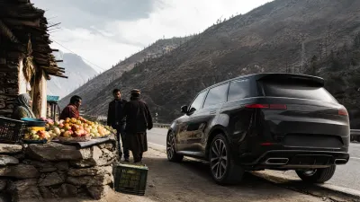 Editorial photo showing a modern luxury SUV parked next to a traditional mountain village fruit stall on the highway.