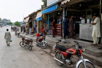 Busy local commercial market street with shops and parked motorcycles in Islamabad.