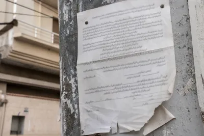 Weathered public notice sheet posted on a wall, photographed at an angle with text kept illegible.