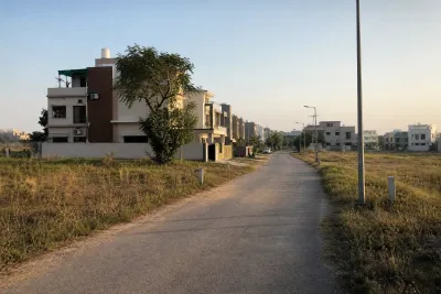 Residential street with a few completed houses alongside undeveloped plots marked by boundary pegs.