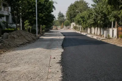 Road construction site with partial asphalt and gravel sections in an Islamabad housing sector.