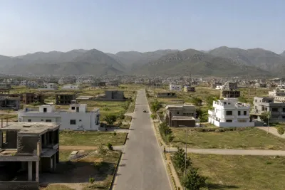 Residential street with a mix of completed and under-construction houses, hills visible in the background.