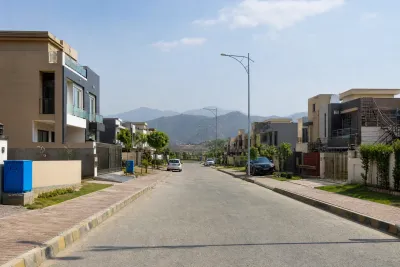 Newly handed-over residential block with paved streets, occupied houses, boundary walls, utility connections and parked cars.