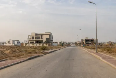 Developing DHA residential sector with paved road, utility poles, open plots, newer houses and ongoing infrastructure work.
