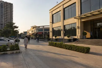 Commercial plaza with shopfronts and a corporate office entrance, moderate pedestrian activity visible.