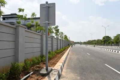 Residential double road with boundary wall and signage post under installation.