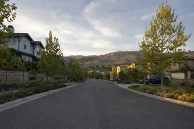 Landscaped residential street with mature trees and hills visible in the background.