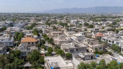Aerial view of a densely developed residential neighbourhood with detached houses, tree-lined streets and the Margalla Hills visible in the background