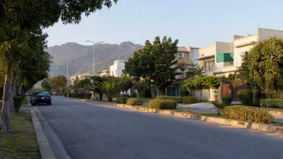Mature tree-lined residential street with landscaped median, established homes and Margalla foothills in the distance.