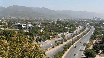Elevated view of a divided, landscaped Islamabad road connecting established residential and urban areas beneath the hills.