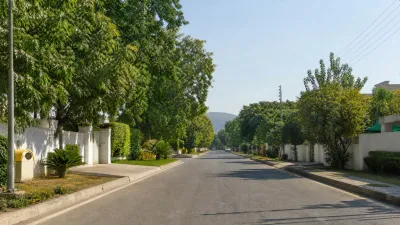 Modern houses and open residential plots along newly developed roads with green hills in the background.