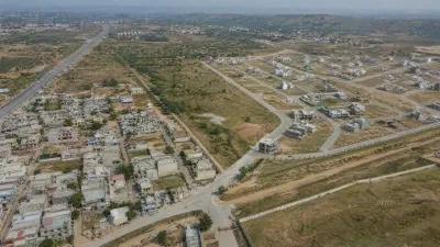 Aerial view of a planned residential area beside highway corridors, open land and newer housing extensions near Islamabad and Rawalpindi.