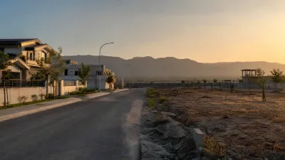 Newer residential road beside open plots, a low boundary wall and distant hills representing the developing Phase 2 edge near Chakri Road.
