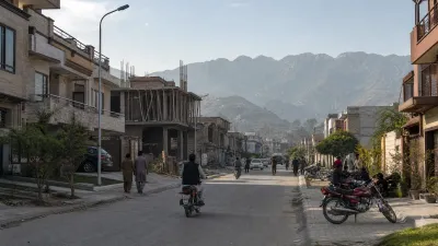 Developing residential street with finished homes, an active construction site and Margalla foothills in the distance.