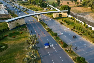 Aerial view of the Park View City entrance road with landscaped medians, security barriers, palm trees, and surrounding green areas.