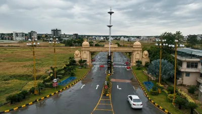 Elevated view of the Grand City Kharian entrance gate with landscaped roads, decorative streetlights, greenery, and residential development in the background.