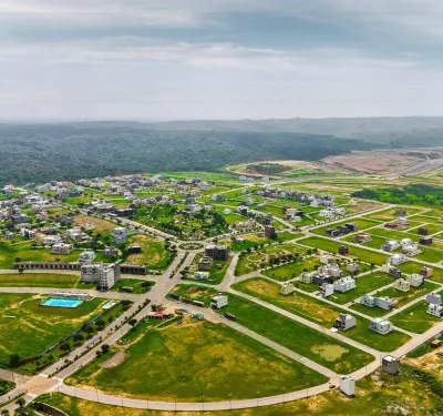 Aerial view of Grand City Kharian featuring residential buildings, wide roads, landscaped green areas, open plots, and hills in the background.