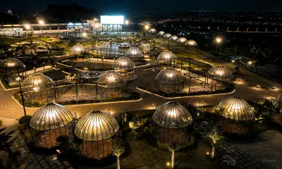 Aerial night view of illuminated dome-shaped pavilions surrounded by landscaped gardens, pathways and warm decorative lighting.