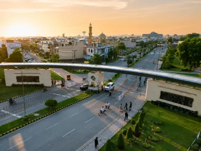Aerial view of WAPDA Town showing a landscaped entrance, wide roads, residential buildings, mosque, and pedestrian bridge at sunset.