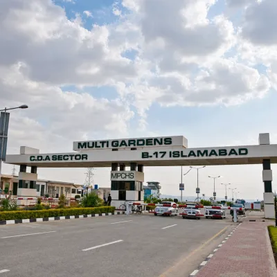 Entrance gate of Multi Gardens B-17 Islamabad with the MPCHS checkpoint, access road, vehicles, and cloudy sky.