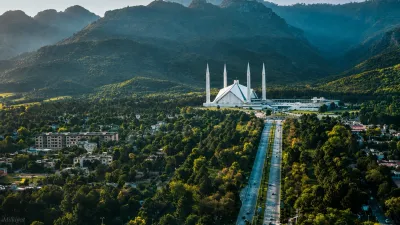 Aerial view of Faisal Mosque in Islamabad surrounded by lush greenery and the Margalla Hills, with a Milkiyat watermark.