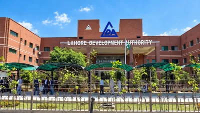 Lahore Development Authority (LDA) headquarters building in Lahore, featuring its red-brick facade, LDA logo, entrance, landscaped grounds, and Pakistan flag under a bright blue sky